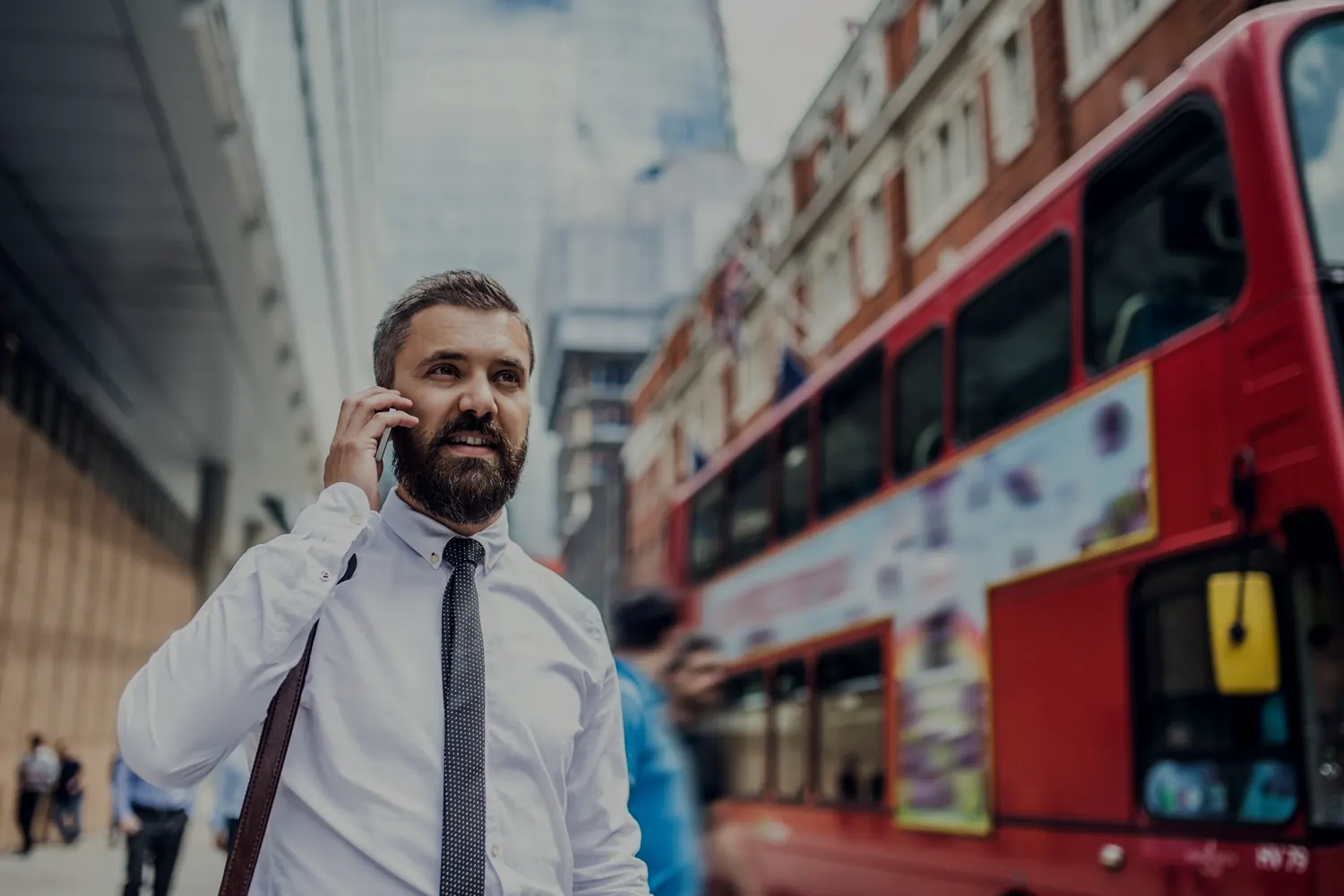 Uomo d’affari al telefono davanti a un autobus rosso di Londra